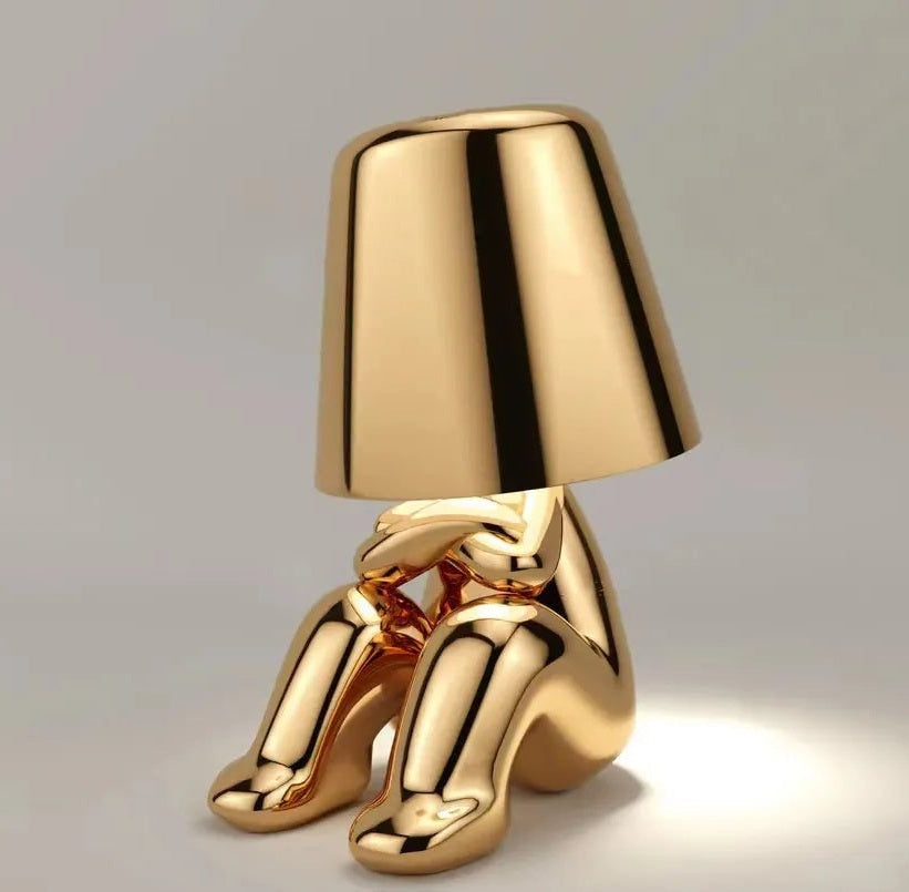 Gold metallic table lamp in the shape of a seated figure with a conical shade