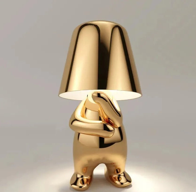 gold aluminum table lamp with a frosted glass shade perched on top of a glossy sculptural figure