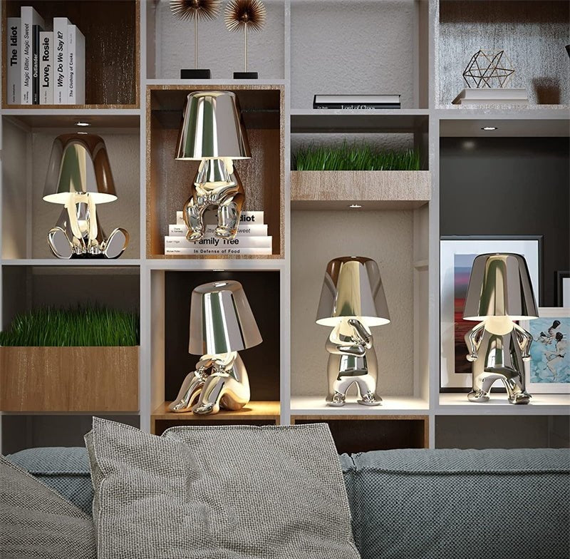 Shiny aluminum table lamps with frosted glass shades displayed on a modular bookshelf with books and plants.