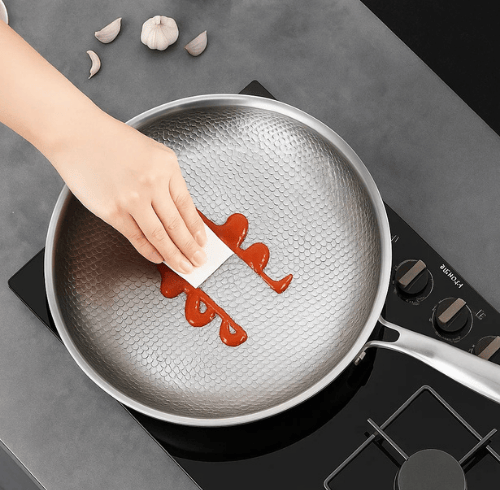 Hand wiping sauce from hammered titanium frying pan on stovetop