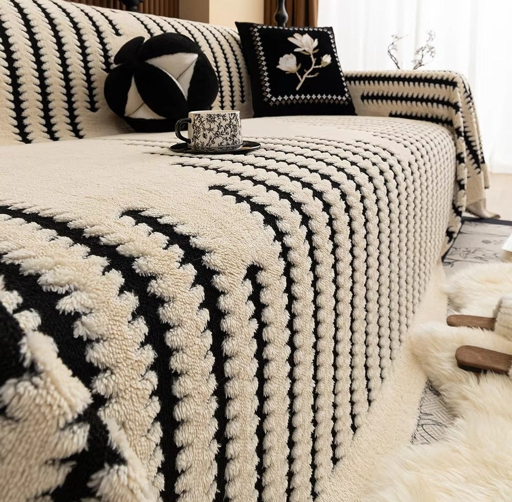 Cream and black plush tufted sofa cover with a linear loop pattern draped over a sofa, accompanied by decorative pillows and a patterned teacup on a saucer