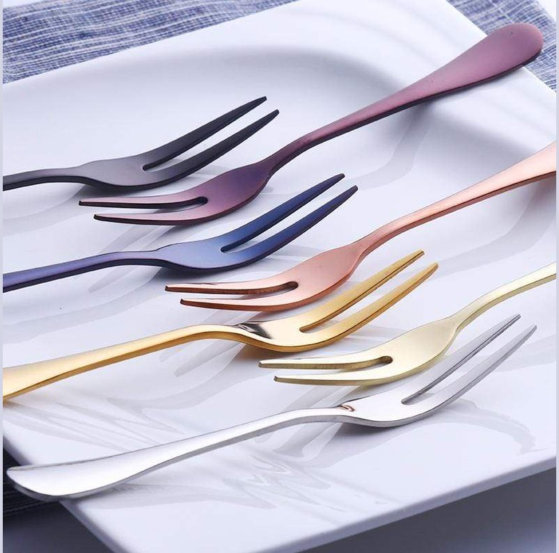 Colorful brushed stainless steel fruit forks in pink purple blue gold and silver arranged on a white plate