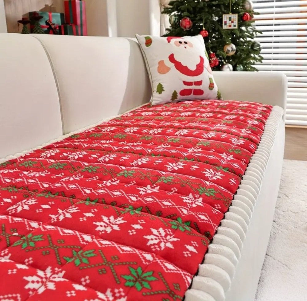 Red quilted Christmas sofa cover with white snowflake pattern on a white sofa, paired with a Santa Claus pillow and a Christmas tree in the background