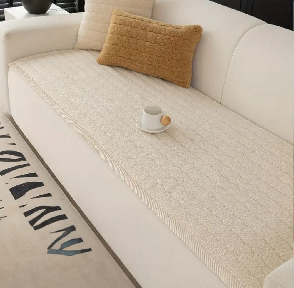 White sofa with a light beige textured plush cover, a tan rectangular pillow and a white pillow, and a small white cup on a saucer placed on the cover