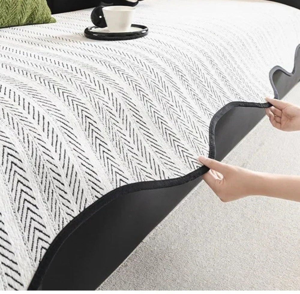 White sofa cover with a black herringbone pattern and a scalloped edge trim being pulled over a sofa