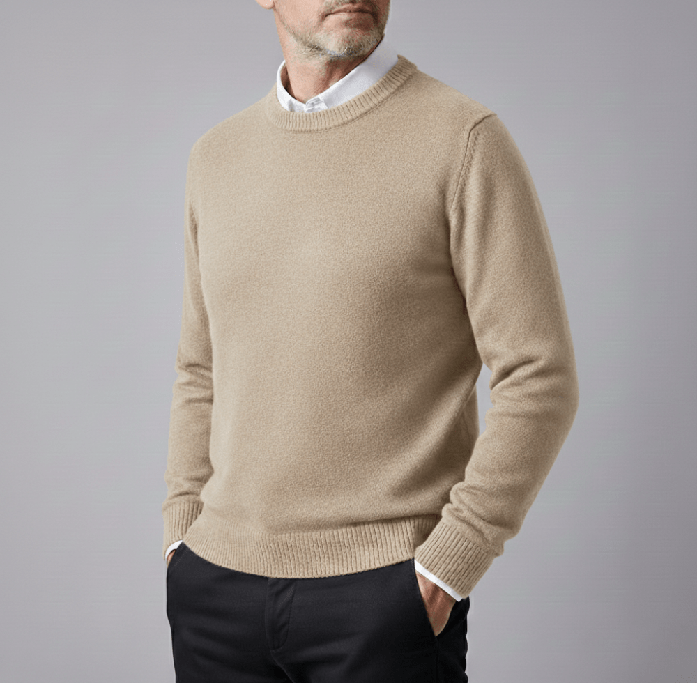 Beige cashmere pullover sweater with a classic crew neck worn by a man, white shirt collar visible at the neckline, ribbed cuffs and hem, and black trousers