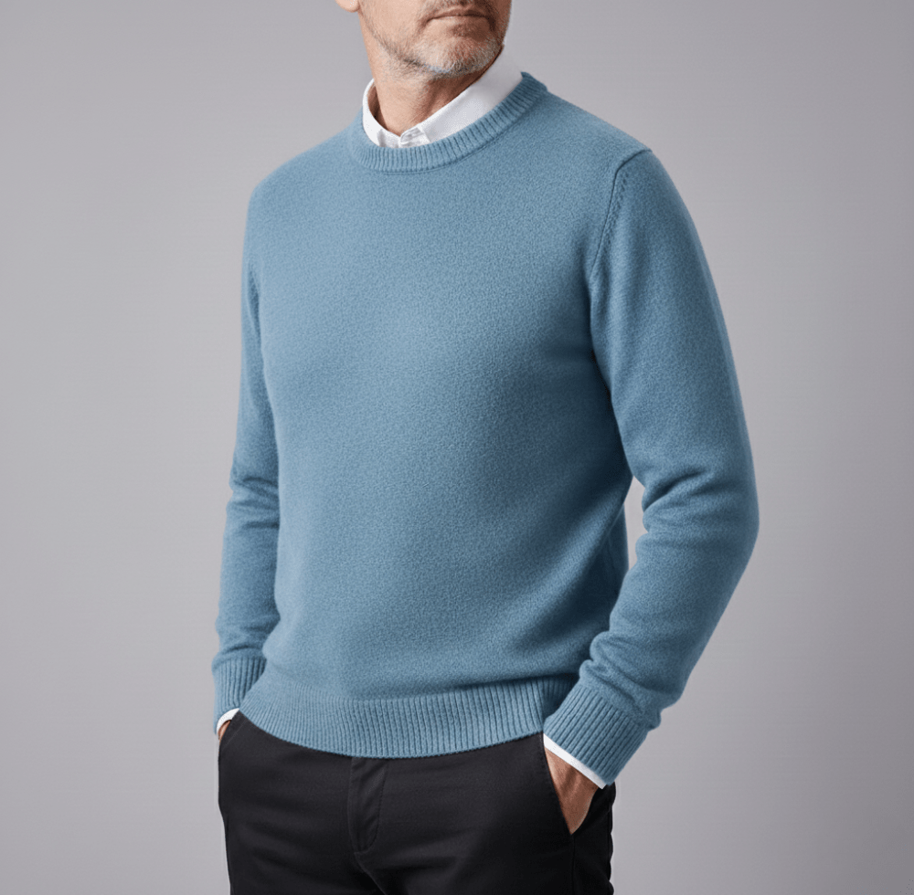 Man wearing a light blue cashmere pullover sweater with a crew neck, ribbed cuffs and hem, white shirt collar visible and black pants
