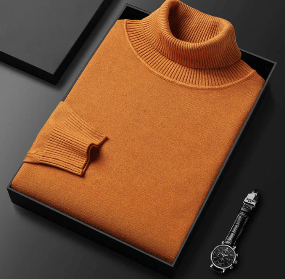 Orange cashmere turtleneck sweater with a ribbed collar folded in a black box on a dark surface beside a metal wristwatch