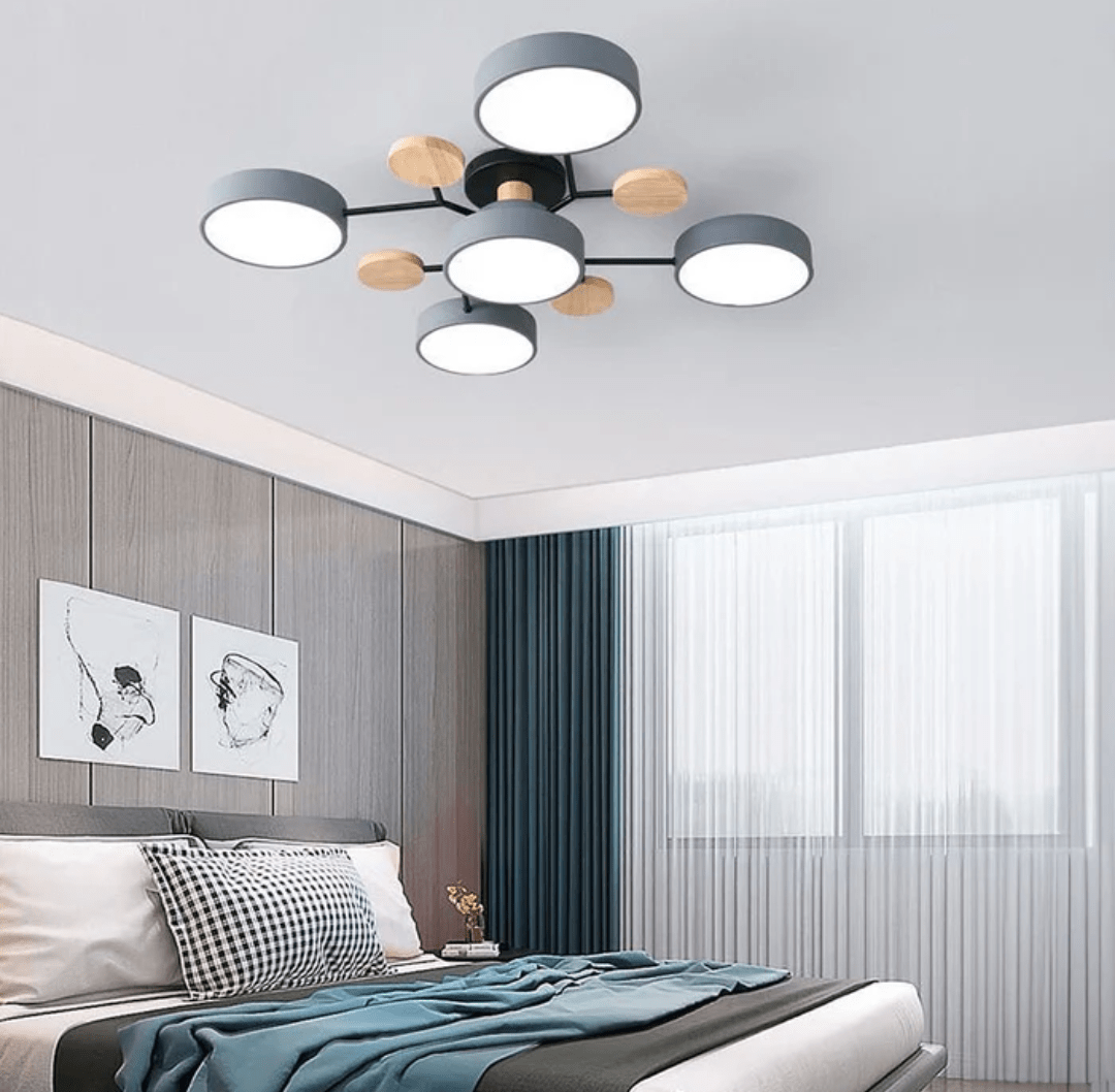 Cluster of round LED ceiling lights with iron gray rims and wood accents above a modern bedroom featuring a wooden paneled wall, a bed with pillows, and a large window with sheer white curtains