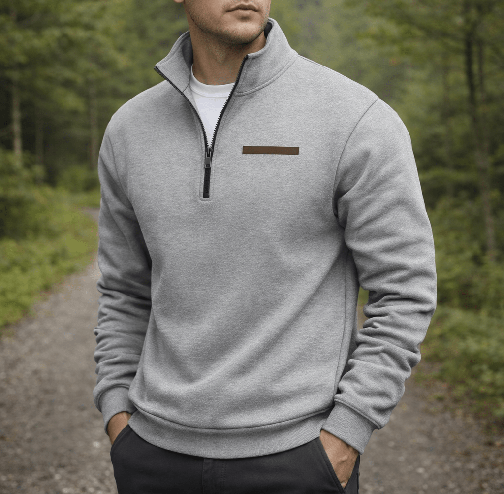 Man wearing a light gray soft fleece blend half zip sweater with a stand up collar and a brown logo patch on the chest outdoors on a forest path