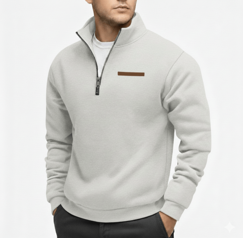 Man wearing a light gray half zip fleece sweater with a zip collar and a small brown chest stripe, hands in pockets.