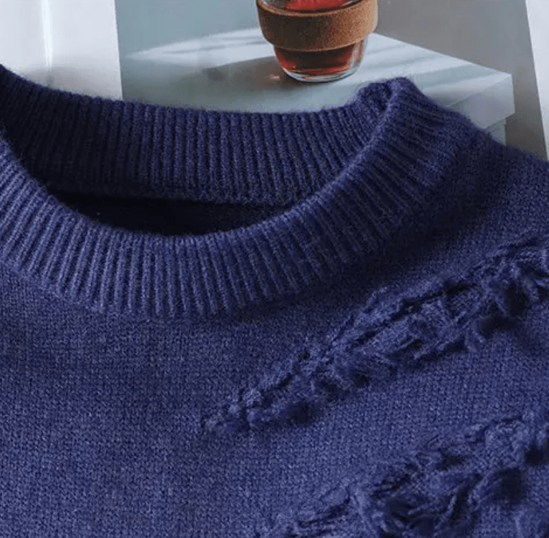 Close up of a navy blue gradient knit crewneck sweater with a ribbed collar and distressed detailing on the front