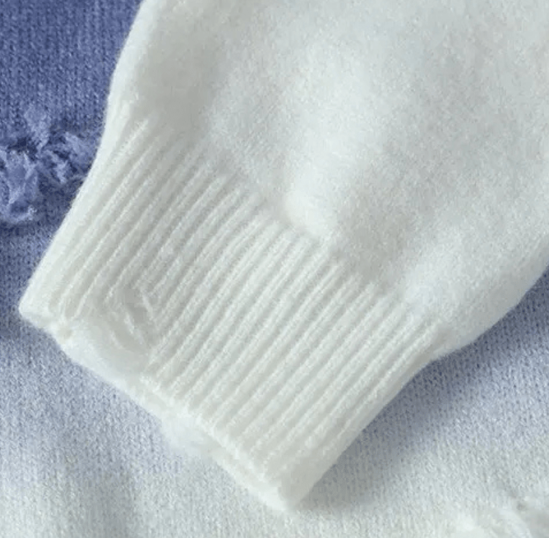 White ribbed sweater cuff with vertical knit ribs against a soft blue knit background
