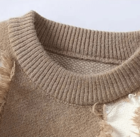 Close up of a beige distressed crewneck sweater showing a ribbed neckline and frayed detailing
