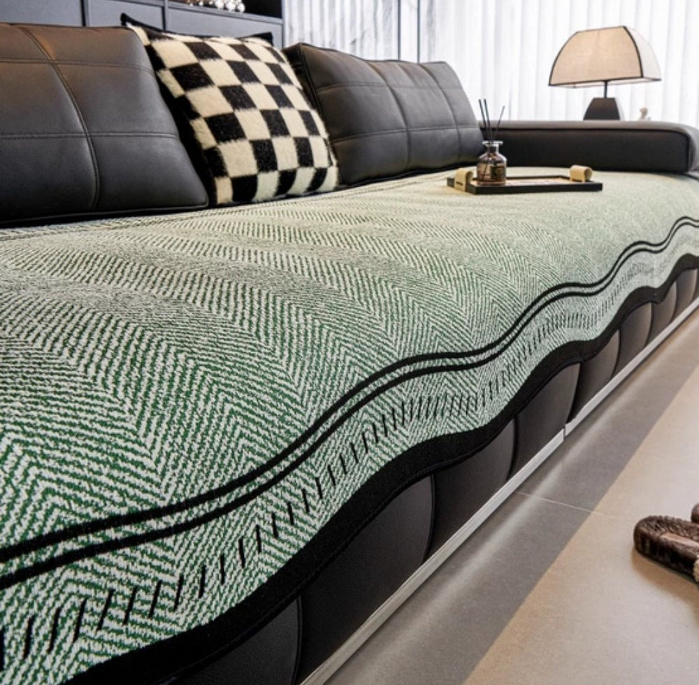 Green patterned microfiber blend sofa cover with a wavy edge and anti slip backing on a black leather sofa in a living room