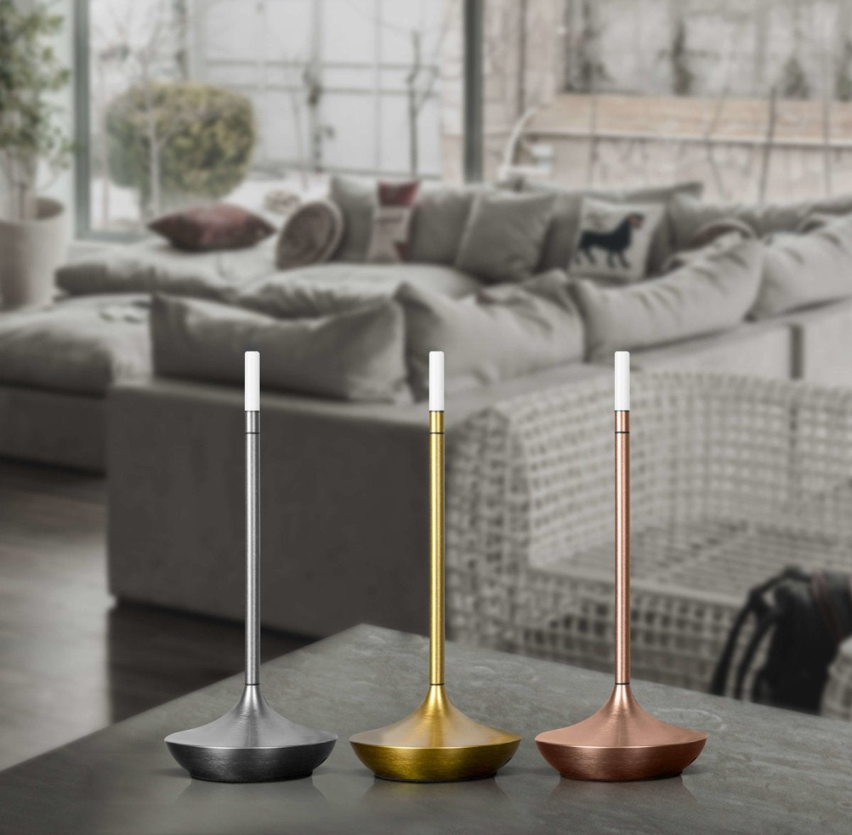 Three tall metal table lamps with white tips and saucer shaped bases in silver gold and copper finishes on a living room coffee table