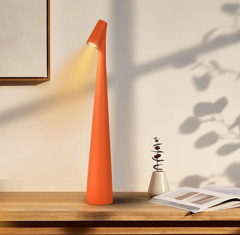 Tall orange conical wireless touch table lamp on a wooden desk with a small beige vase and an open magazine nearby.