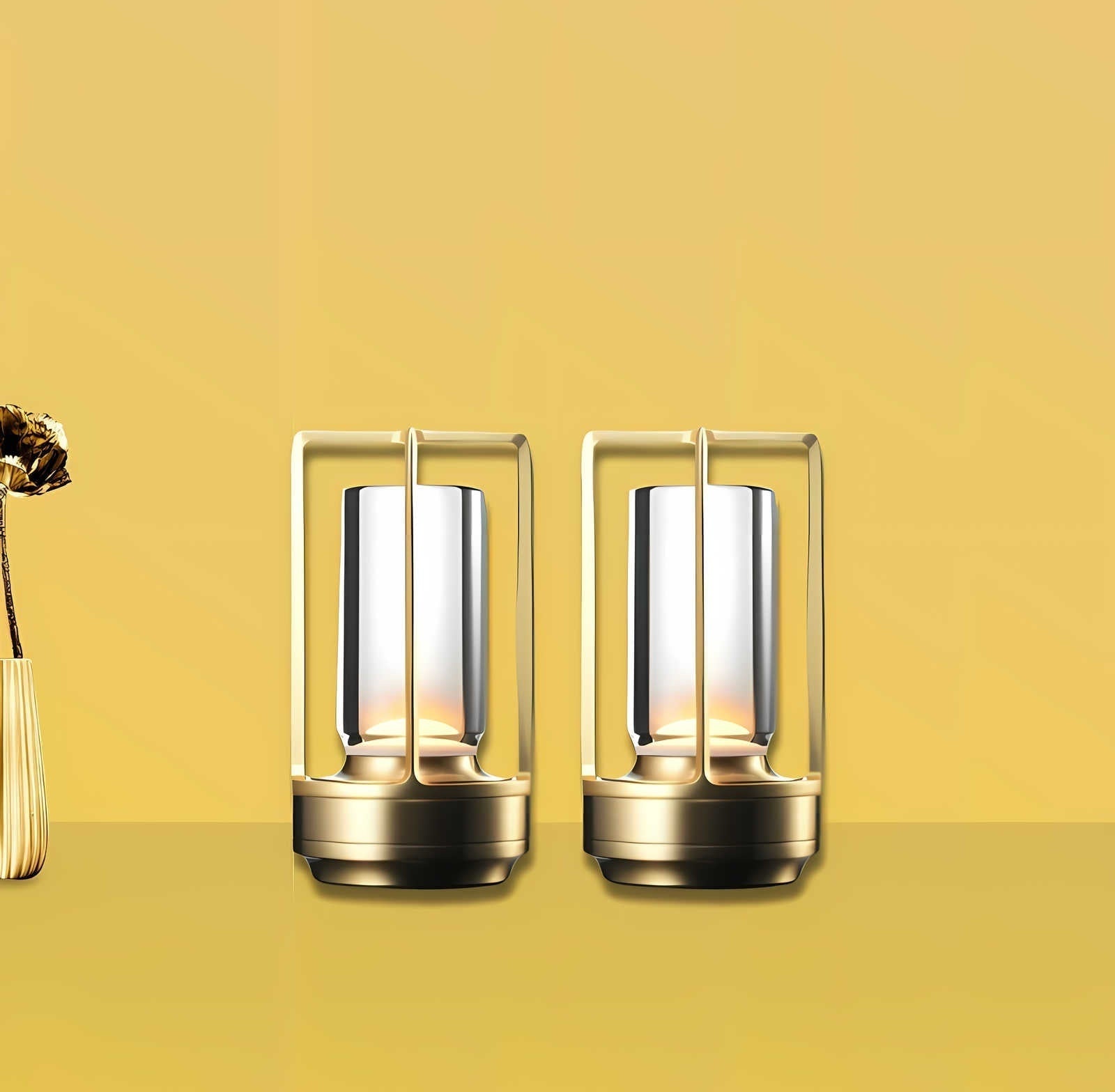 Two gold metal framed cordless lantern table lamps with glass cylinders emitting warm light on a yellow background with a dried flower vase on the left