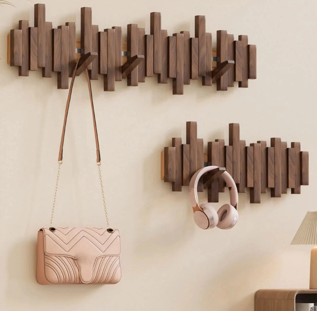 Sonata wall coat rack made of solid wood in a natural finish with five hooks mounted on the wall, a pink handbag hangs from a chain, and pink headphones hang on the rack