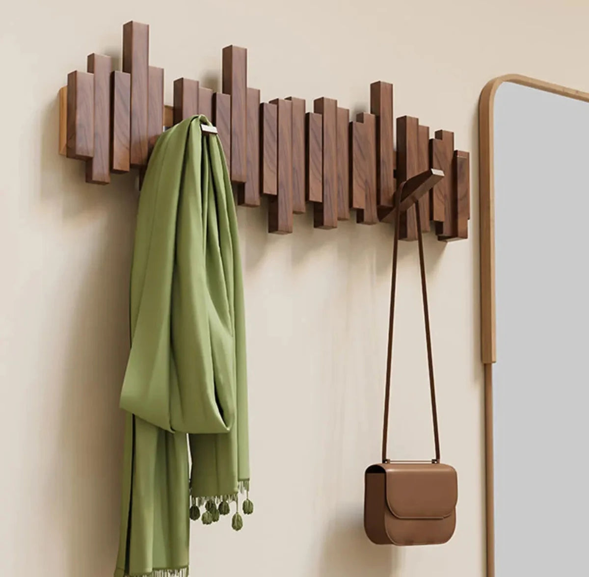 Natural finish solid wood wall coat rack with five rectangular hooks, a green scarf hangs on one hook and a brown shoulder bag hangs from another