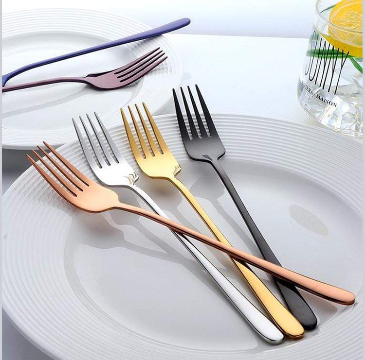 Five mirror finished forks in rose gold silver gold and black arranged on a white plate with a glass of lemon water in the background