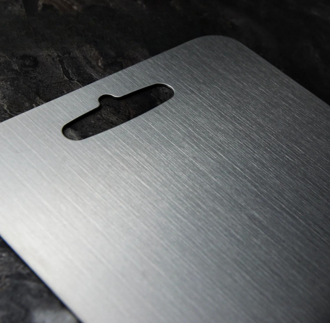 Aegis titanium cutting board with a brushed metal surface and an oval handle slot