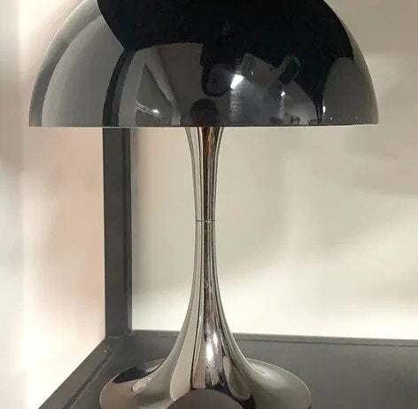 Modern chrome table lamp with a curved stem and a glossy black dome shade on a shelf