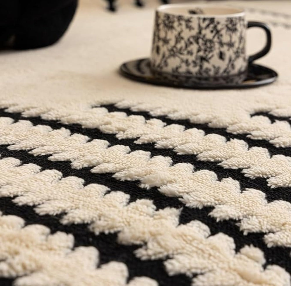 A black and white patterned cup on a black saucer sits on a cream and black tufted rug with a textured looped pattern