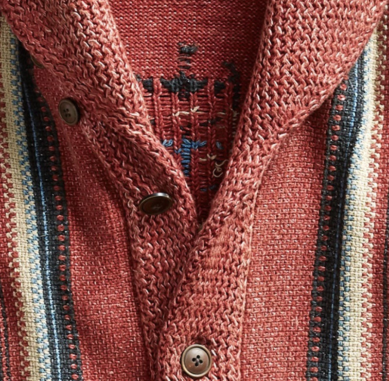 Close up of a red jacquard knit cardigan with a lapel collar and brown button closure and striped trim along the front edges