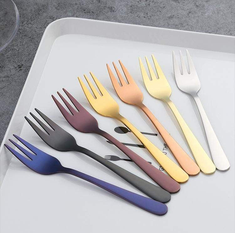 Colorful plated stainless steel salad forks arranged in a row on a light gray tray showing blue, purple, gray, gold and silver tones