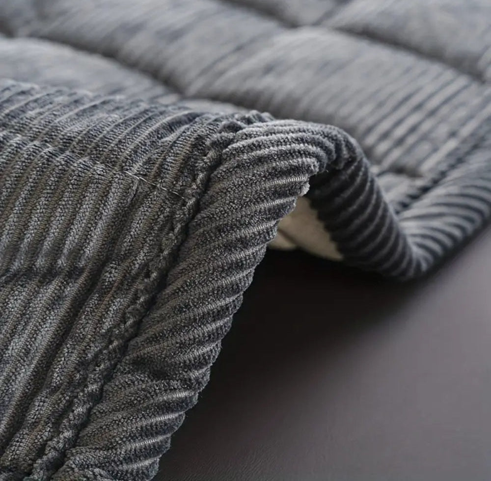 Close up of a gray quilted microfiber sofa cover with a folded edge and ribbed texture