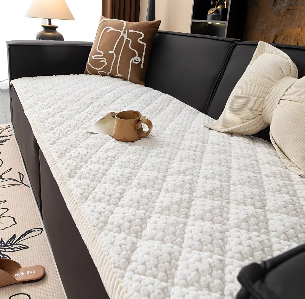 White bubble quilted sofa protector slipcover on a dark sofa with beige cushions and a brown mug resting on top