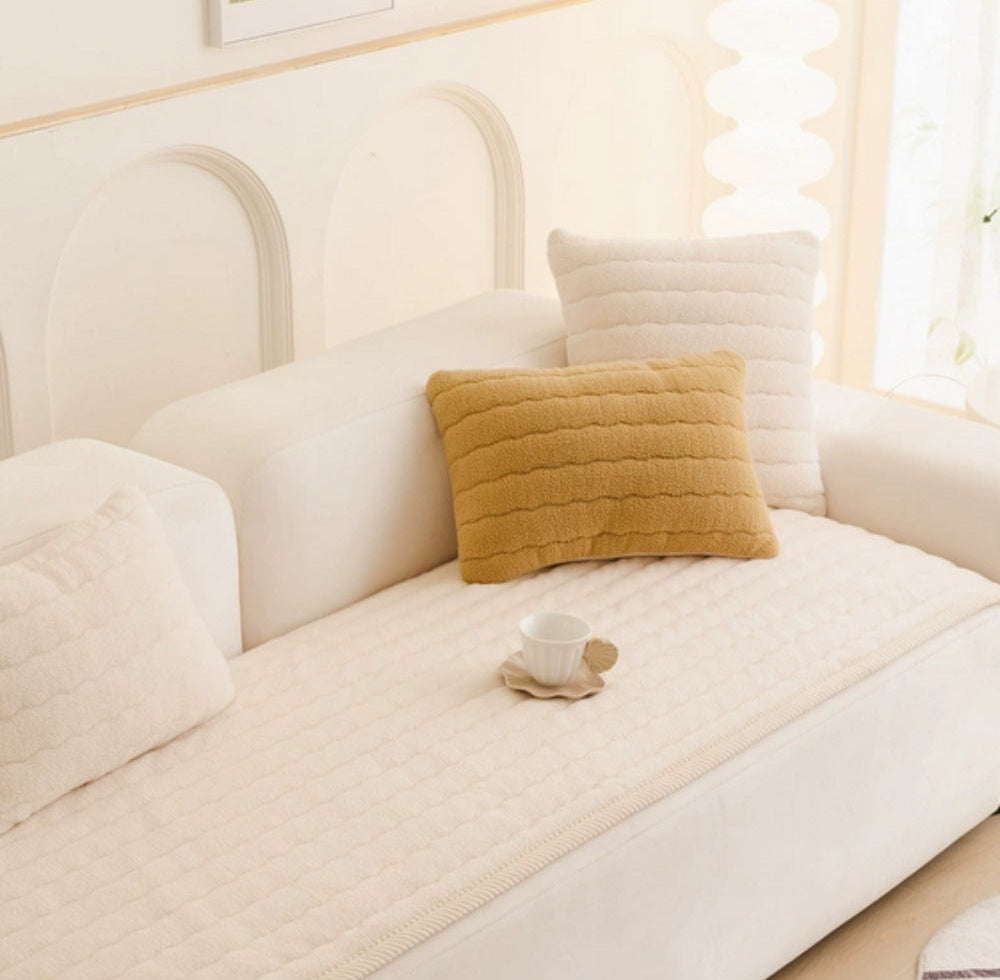 Cream sofa with a plush microfiber blend quilted cover, tan and white textured pillows, and a small white teacup on a saucer resting on the cover