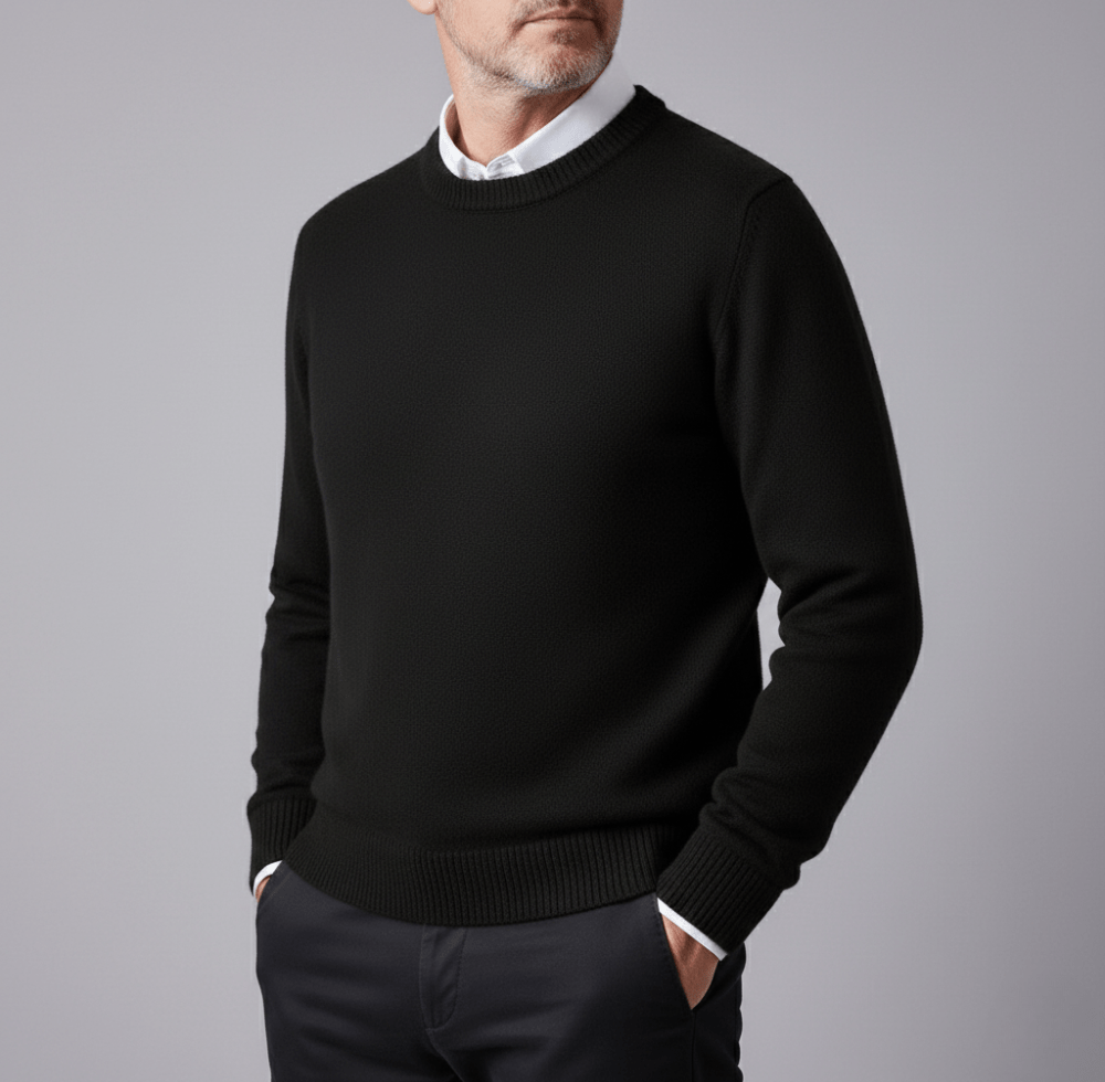 Man wearing a black cashmere pullover sweater with a classic crewneck and a white shirt collar visible, standing with hands in pockets