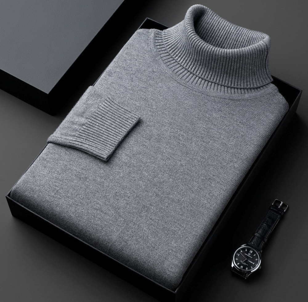 Gray cashmere turtleneck sweater folded inside a black box with a ribbed collar and cuff, and a black leather watch placed beside the box.