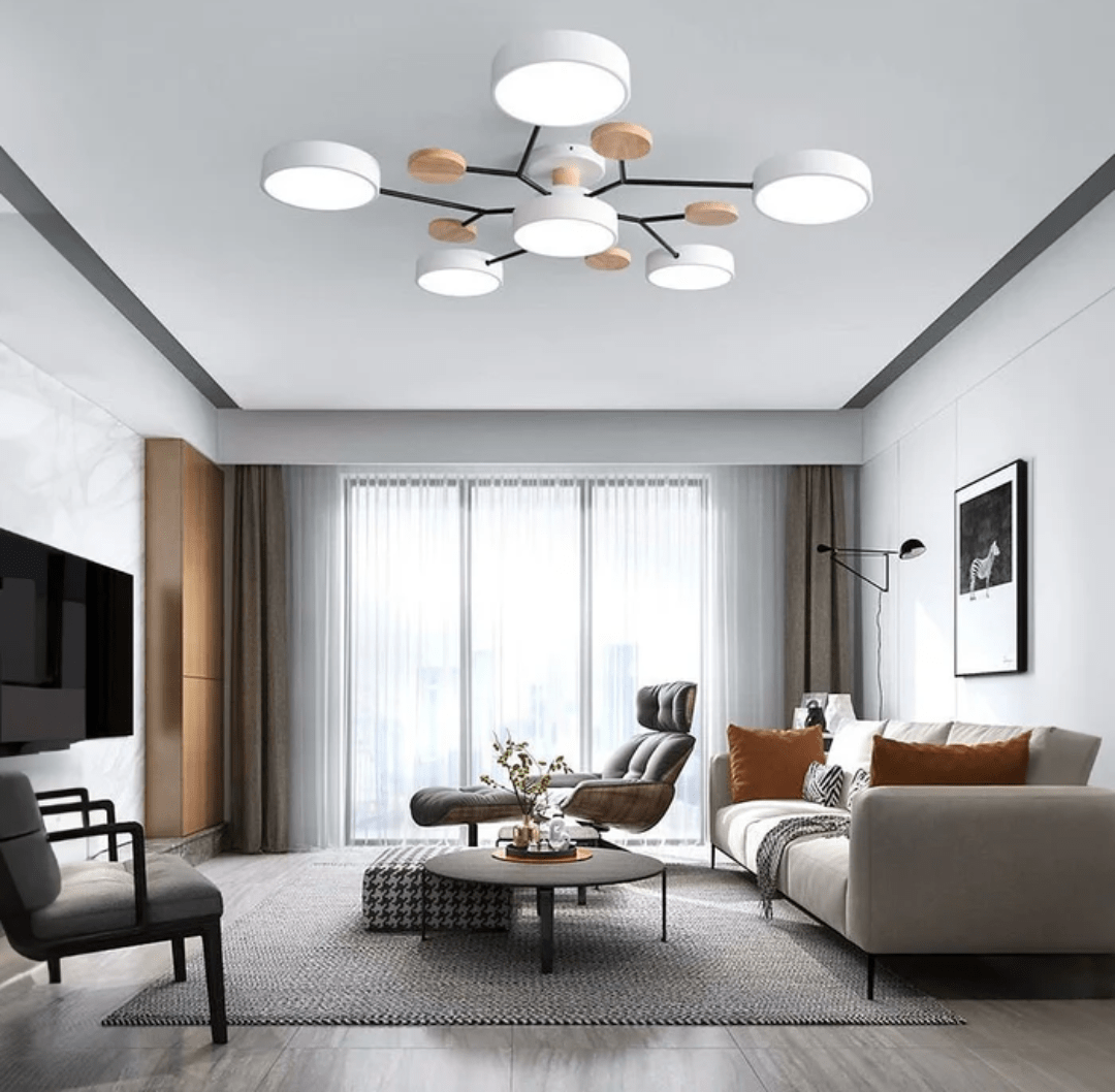 Living room with a modern round LED ceiling light featuring white circular panels and wooden accents, a gray sofa with orange cushions, a lounge chair, a coffee table, and large windows with sheer curtains.