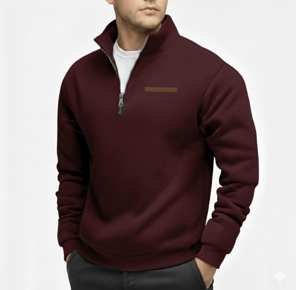 Man wearing burgundy half zip fleece sweater with a zip collar and a small tan logo on the left chest white shirt underneath with hands in pockets