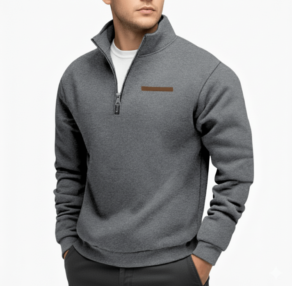 Man wearing a gray fleece half zip sweater with a raised collar and white shirt underneath, zipper partially zipped and a brown rectangular emblem on the left chest