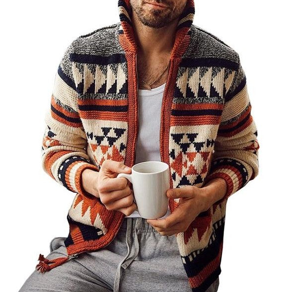 Man wearing a geometric knit zip cardigan sweater jacket with an open front zipper in orange navy and cream pattern, holding a white mug