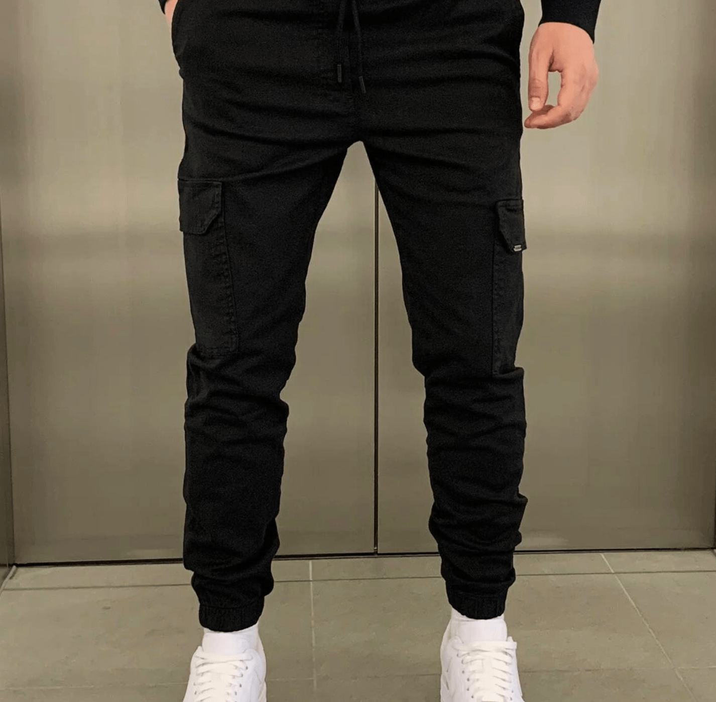 Black cargo jogger pants with a relaxed fit and elastic waistband, cargo pockets on the thighs, elastic cuffs and white sneakers