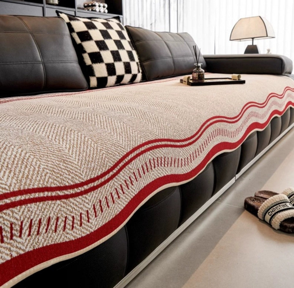 Sofa covered with a beige woven throw featuring a red wavy edge on a black leather couch with a black and white checkered cushion and a small tray on the armrest