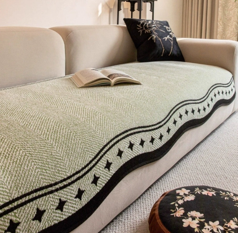 Beige sofa with Seabrook microfiber cover featuring a woven pattern and a black wavy edge border with star shaped accents, an open book rests on the cover beside a dark decorative pillow and a floral round ottoman nearby.