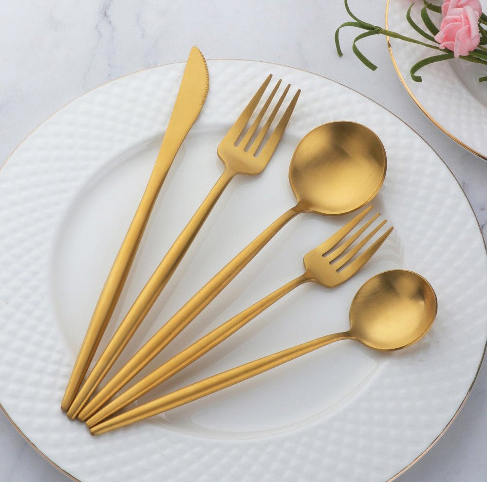 Gold plated stainless steel cutlery set with slim curved handles laid out on a white textured plate