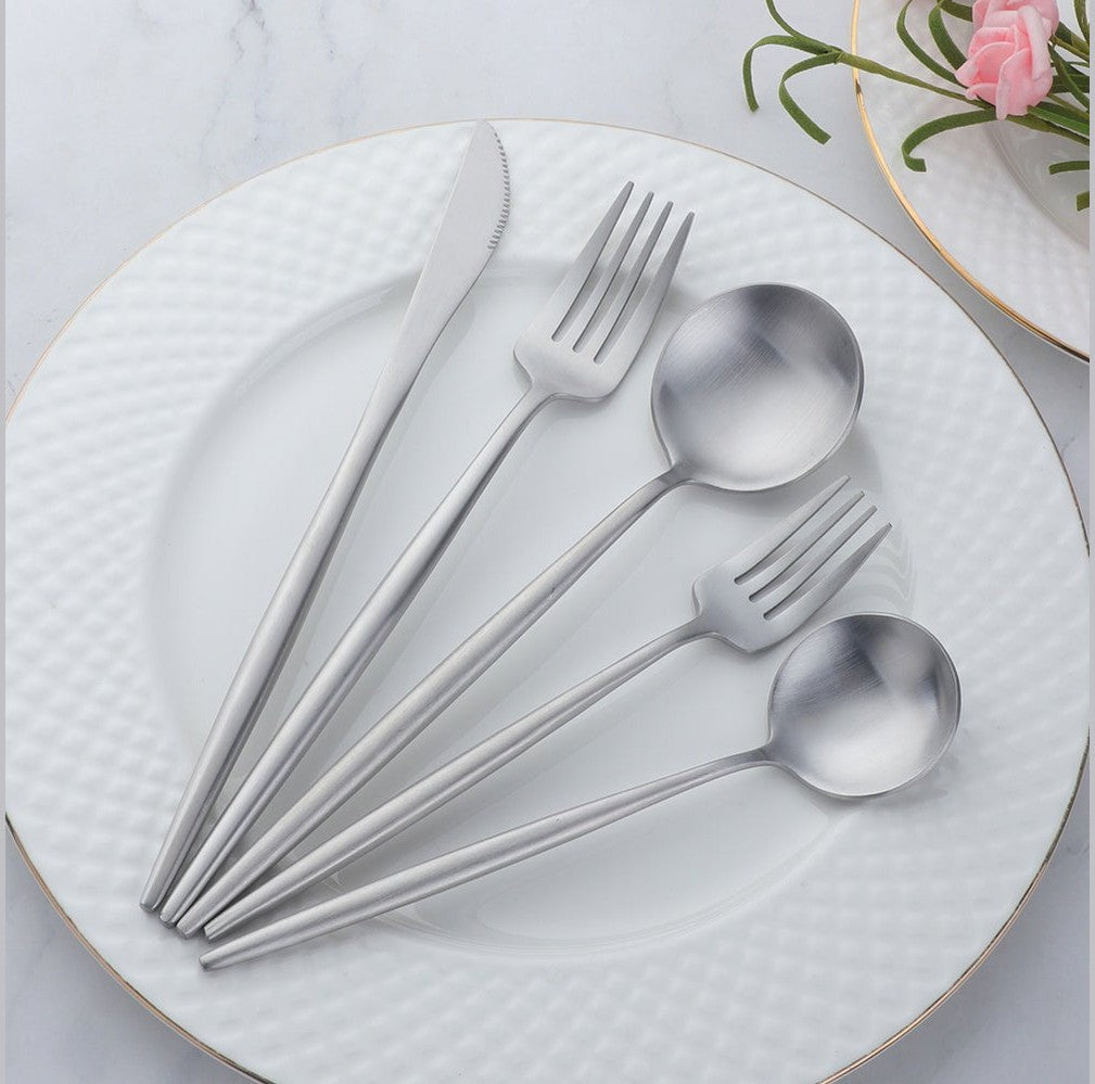 Stainless steel cutlery with slim curved handles arranged on a white textured plate, including knife forks and spoons