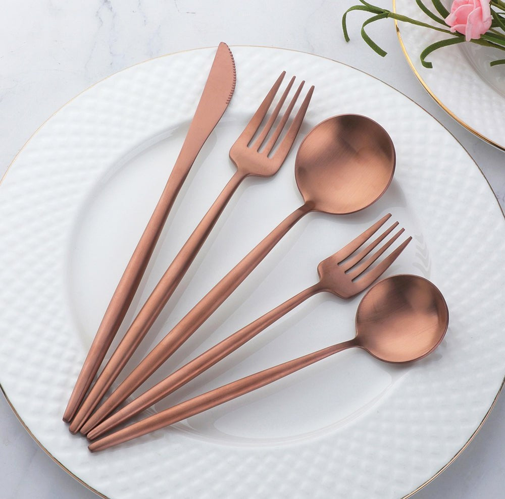 Sevilla Curve copper plated stainless steel cutlery set with slim curved design displayed on a white plate