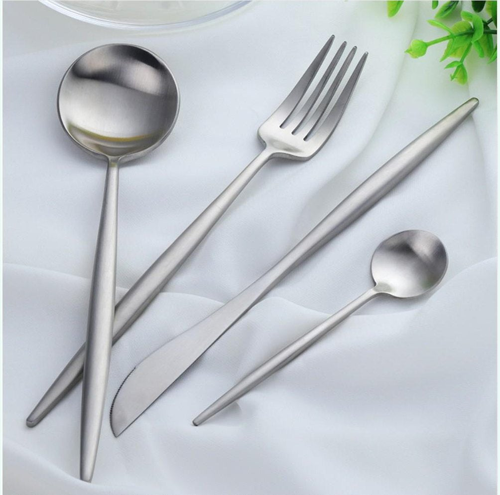 Stainless steel cutlery set with slim curved handles including a large spoon a fork a knife and a small spoon on a white fabric background