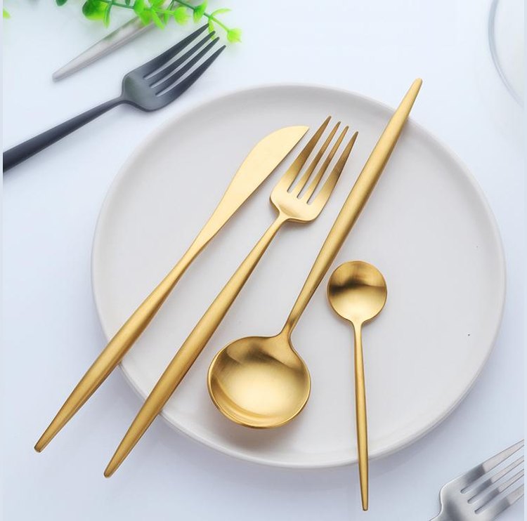 Gold plated stainless steel cutlery set with slim curved handles displayed on a white plate.