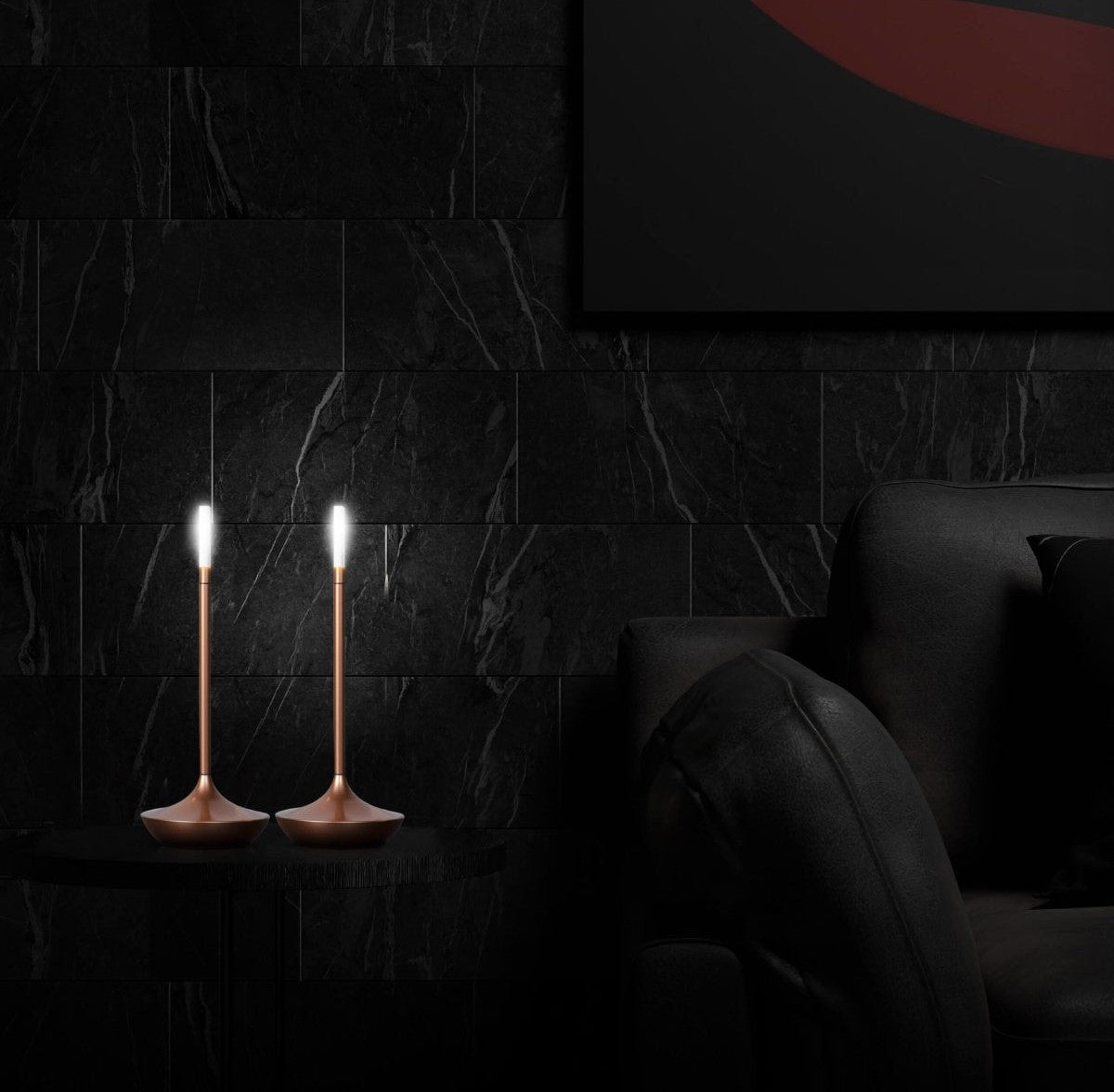 Two slender copper colored LED table lamps with wide rounded bases sit on a small black table against a dark marble wall beside a black sofa, emitting white light.