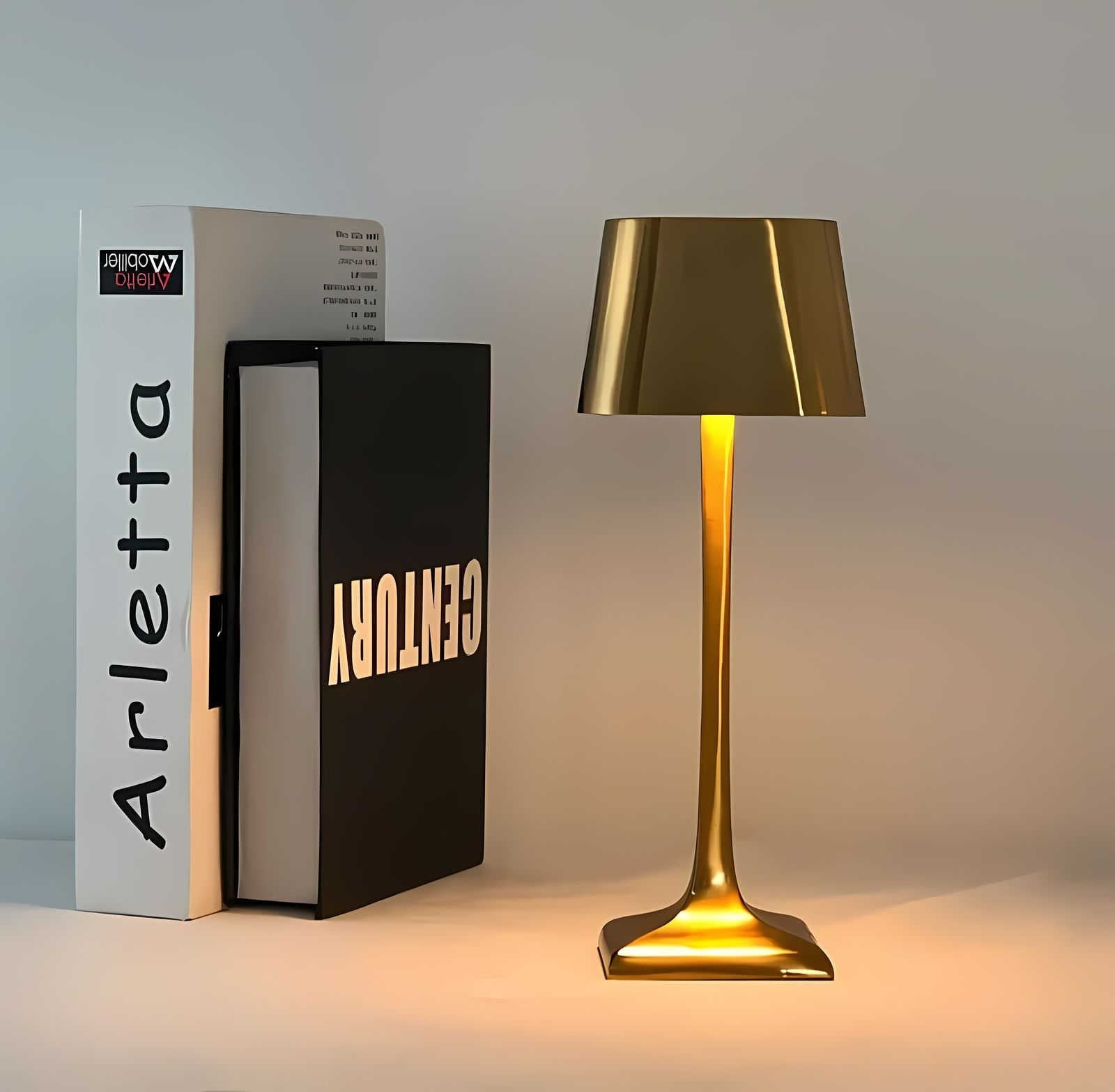 Gold cordless table lamp with a slender stem and wide metallic shade emitting a warm glow beside white and black packaging boxes