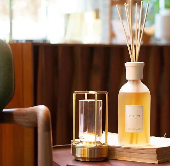 Solaran cordless lantern table lamp with crystal glass and gold metal frame sits on a wooden table beside a reed diffuser bottle with sticks.